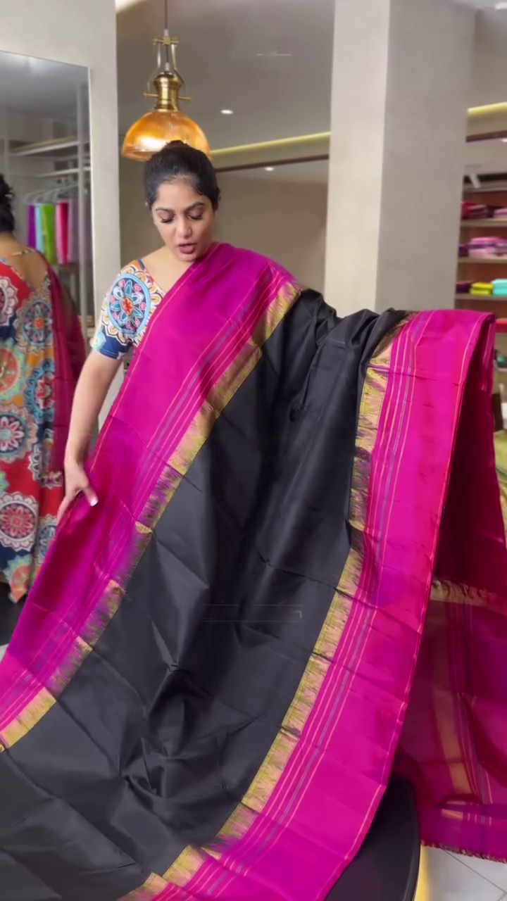 Woman holding a black saree with pink border in a store setting